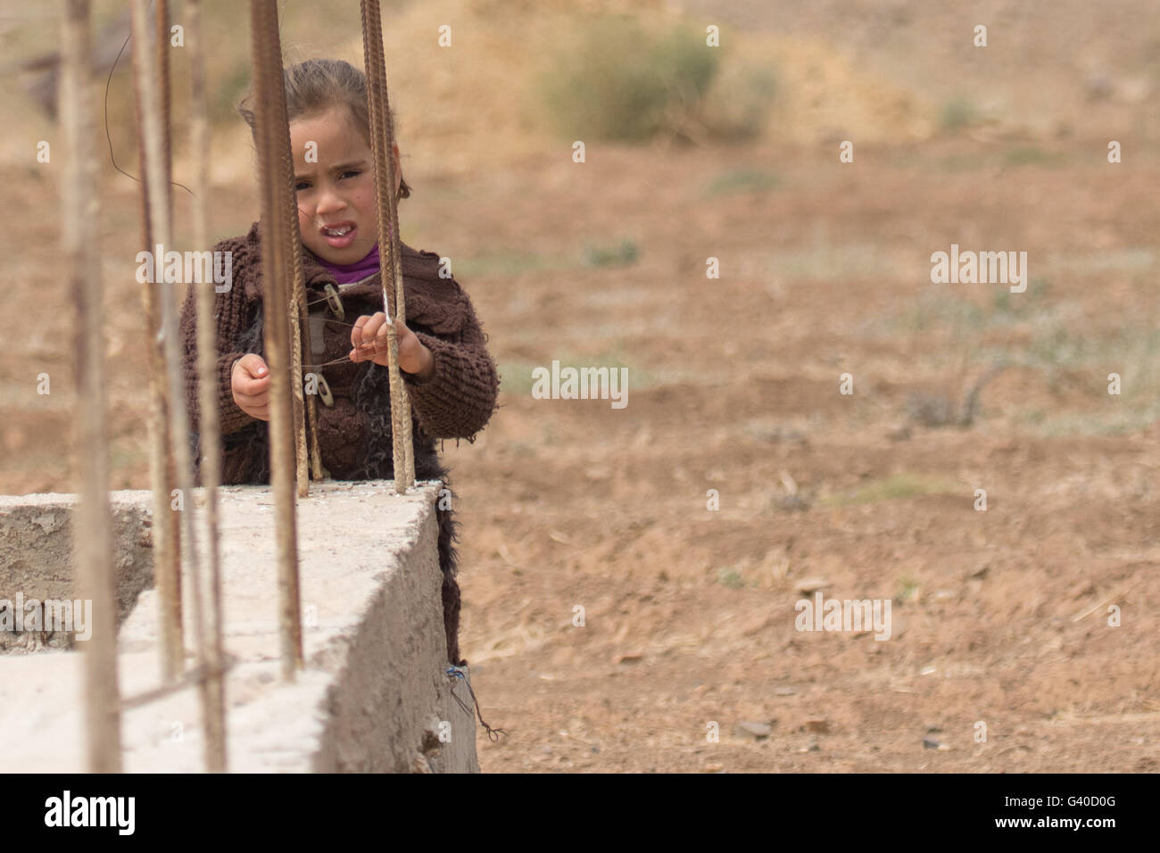 Moroccan girl peeping through bars on concrete post, looking curious. Stock Photo