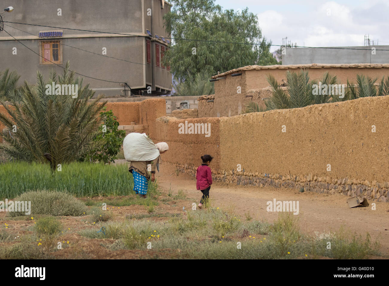 Backview of Morrocan woman with heavy load and small child returning to house, Stock Photo