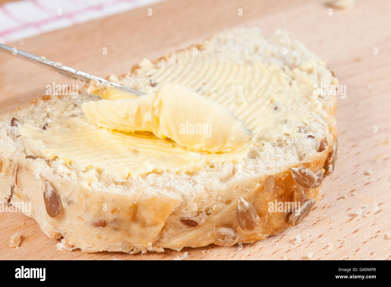 Slice of honey topped and sunflower seeded bread getting buttered on a wooden chopping board Stock Photo