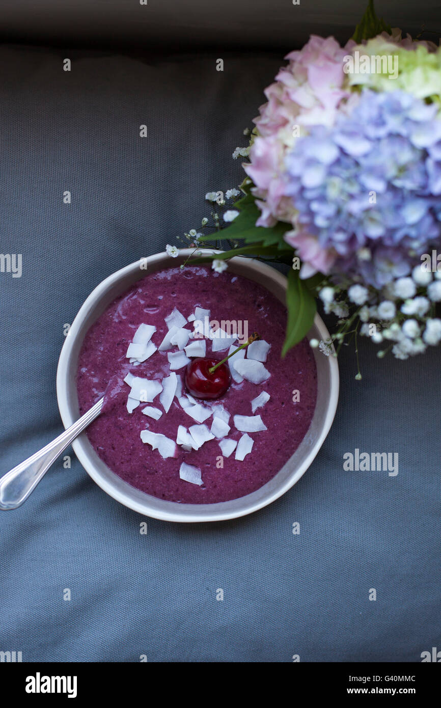 Cherry coconut smoothie in a grey bowl topped with coconut flakes and one whole cherry Stock Photo