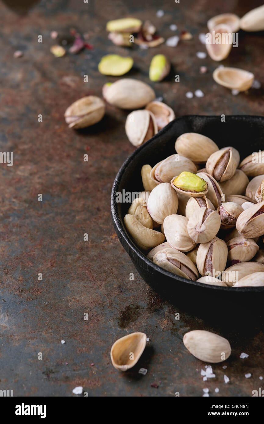 Salted roasted pistachios nuts with shell and salt in in black small castiron pan over old