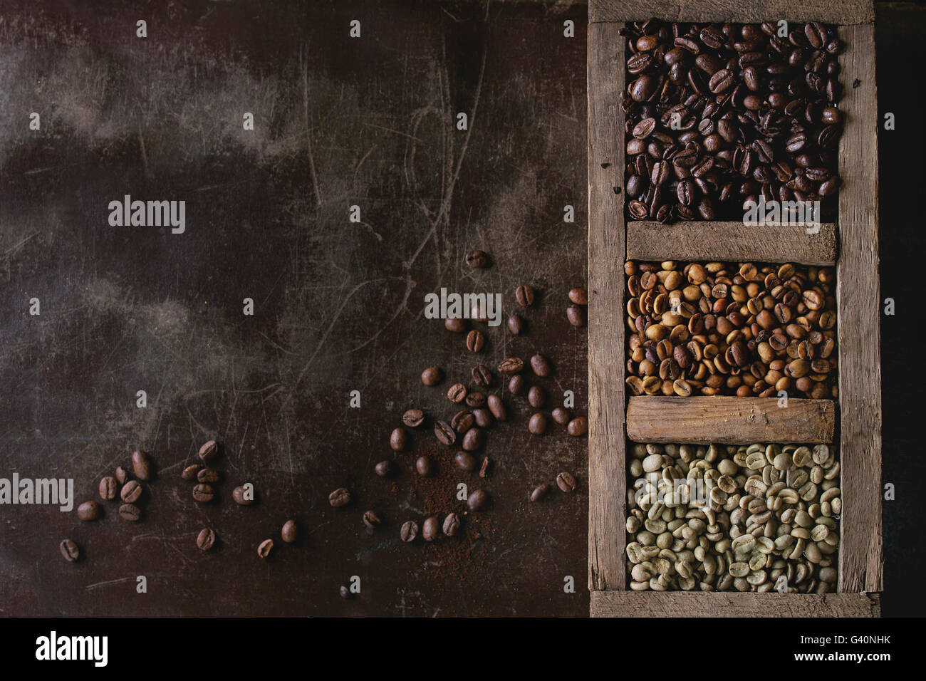 Green and brown decaf unroasted and black roasted coffee beans in old wooden box over dark brown textured background. Top view. Stock Photo