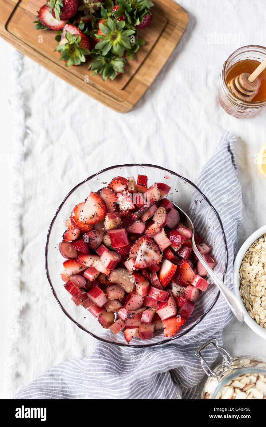 A big bowl of sliced strawberries and rhubarb is sprinkled with poppy seeds and photographed from the top view. Stock Photo