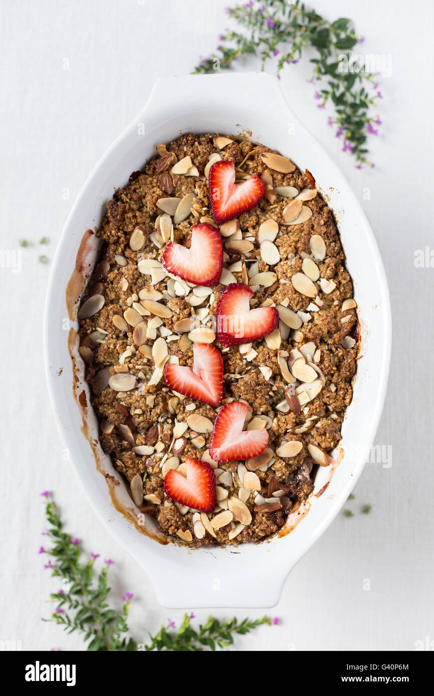 A large oval bowl (surrounded with flowers) of Strawberry and Rhubarb Breakfast Oat Crisp is photographed from the top. Stock Photo