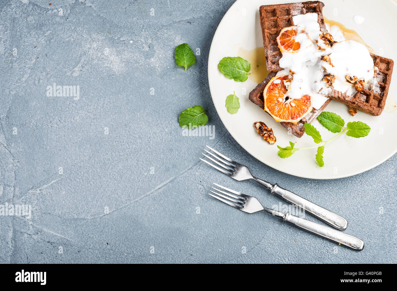 Belgian soft waffles with blood orange, cream, marple syrup and mint on white plates over concrete textured background. Top view Stock Photo