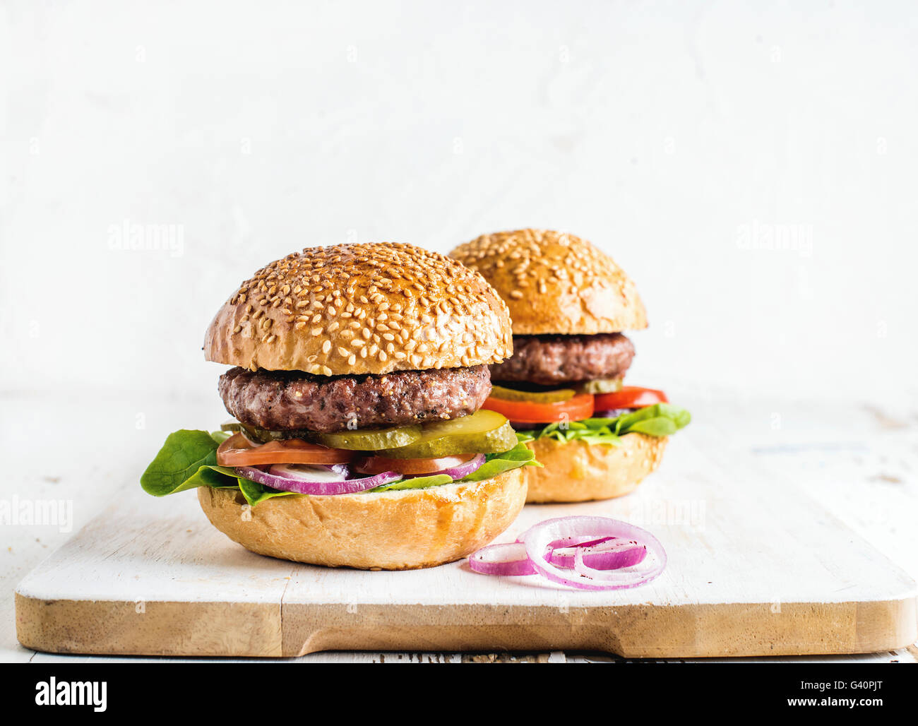 Fresh homemade burgers on wooden serving board with onion rings. White background, selective focus, copy space Stock Photo