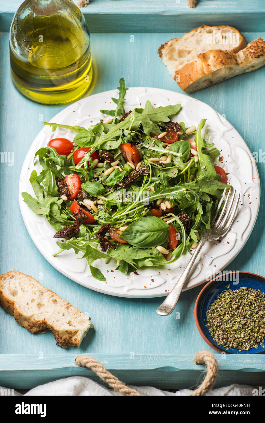 Salad with arugula, cherry tomatoes, pine nuts and herbs on white ceramic plate over blue wood background, selective focus Stock Photo