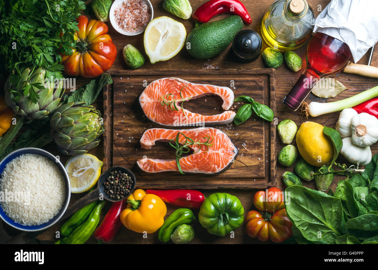 Raw uncooked salmon steak with vegetables, rice, herbs, spices and wine bottle on chopping board over rustic wooden background, Stock Photo
