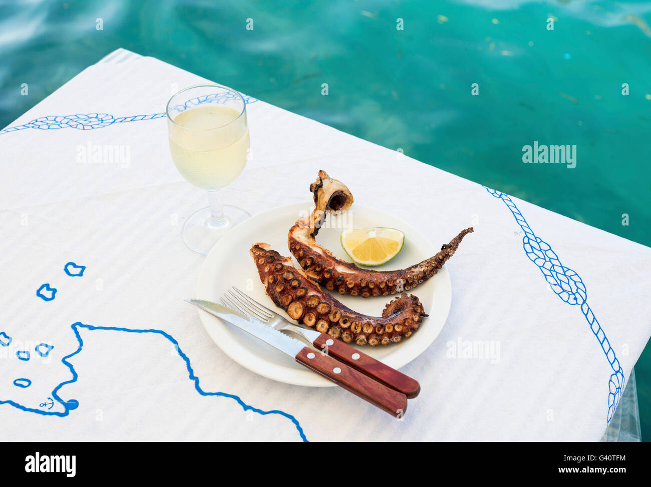 Grilled octopus and white wine glass on a table at the sea coast in small restaurant on a Greek island of Kastelorizo Stock Photo