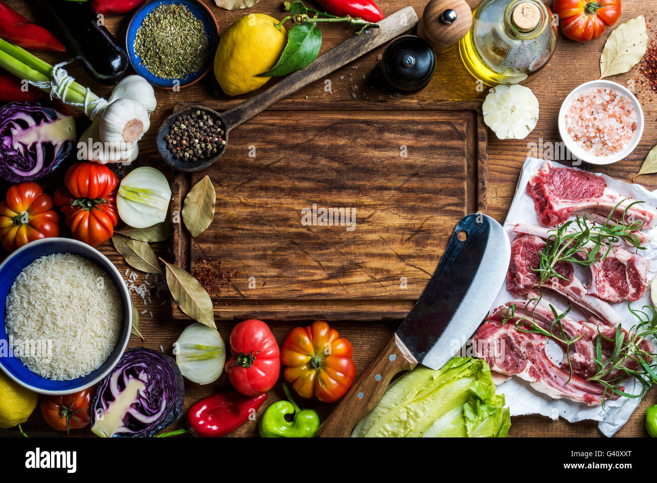 Ingredients for cooking healthy meat dinner. Raw uncooked lamb chops with vegetables, rice, herbs and spices over rustic wooden Stock Photo