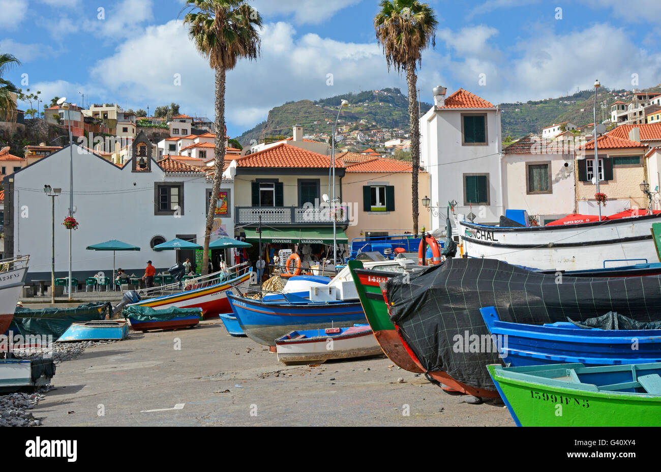Fishing boats drawn up on beach and slipway at Camara de Lobos in Madeira, Portugal. With people in restaurants behind Stock Photo