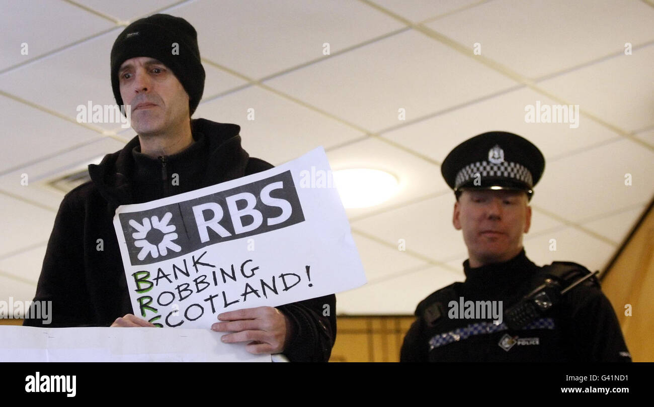 A police office watches a member of protest group Citizens United Against Cuts to Public Services, during a protest calling for banks to be regulated and bonuses eliminated, inside a Royal Bank of Scotland building in Glasgow, Scotland. Stock Photo