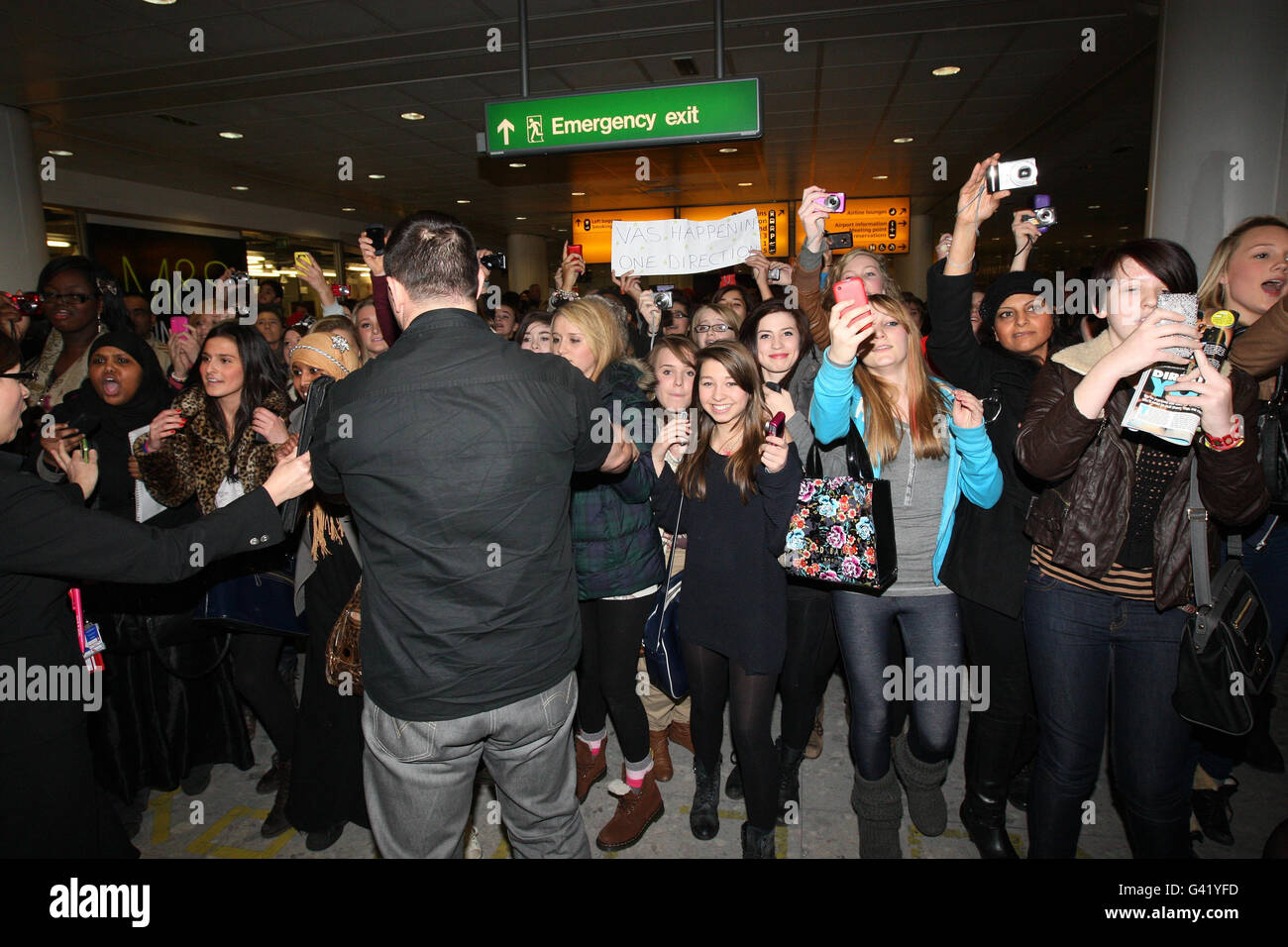Fans pursue X Factor boy band stars One Direction, as they arrive back from LA into Heathrow Airport. Stock Photo