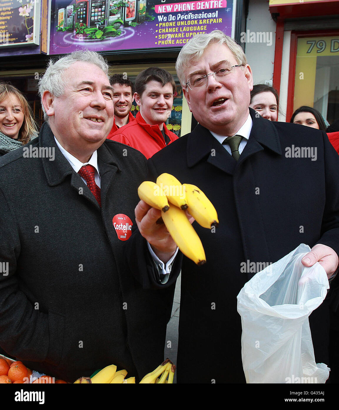 Irish Labour leader Eamon Gilmore (right) with candidate Joe Costello (left) buys a bunch of bananas from a vendor on Moore Street in Dublin, while canvassing in Dublin City centre. Stock Photo