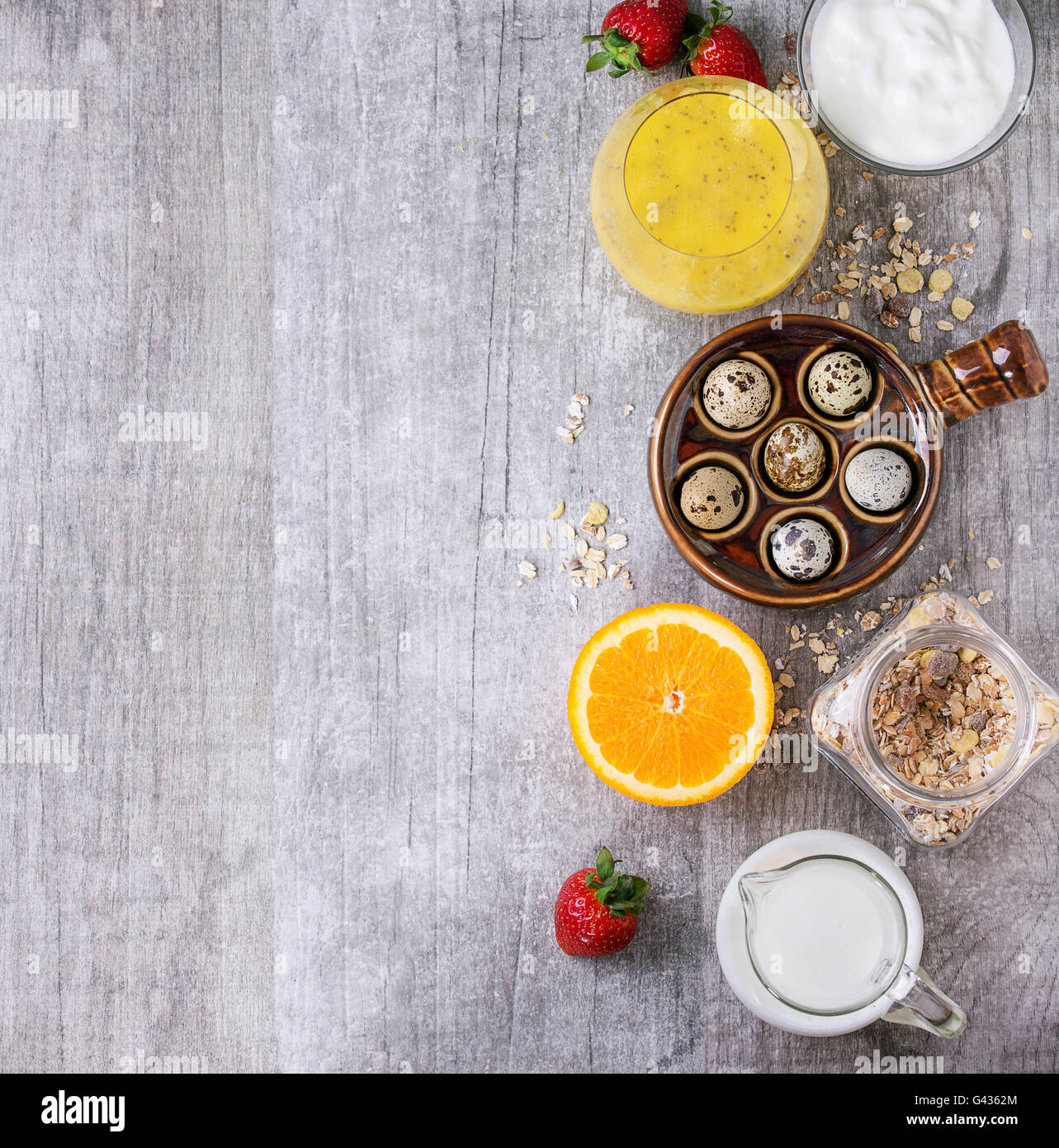 Food concept background with ingredients for healthy breakfast. Quail eggs, muesli flakes, yogurt, mango smoothie, sliced orange Stock Photo