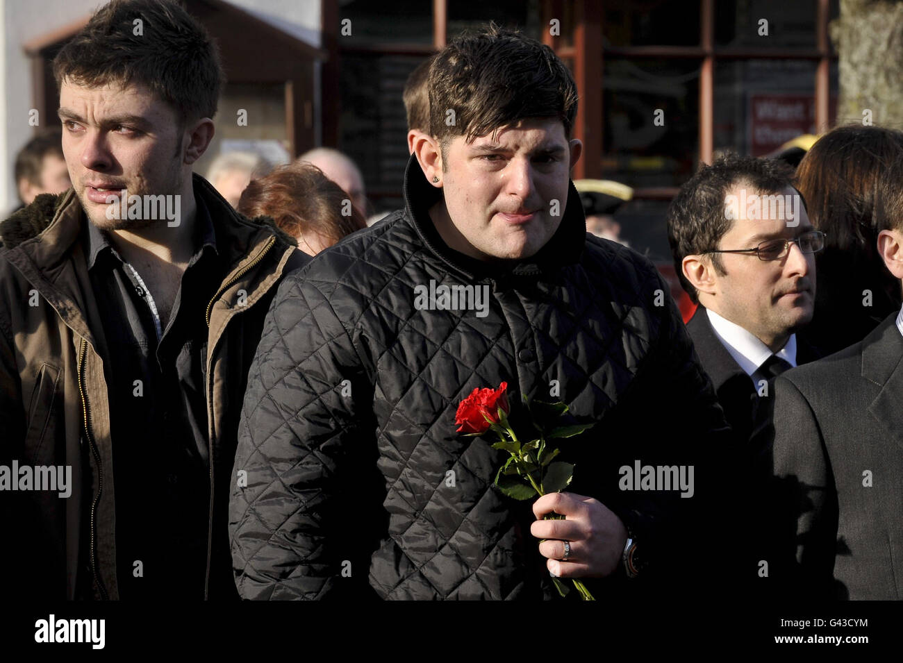 A man in the crowd on Wootton Bassett High Street holds a single red rose and peeks out to watch as the hearse carrying the coffin of Private Martin Bell of the 2nd Battalion Parachute Regiment, passes through Wootton Bassett as he is repatriated back to the UK. Stock Photo