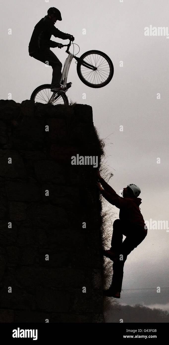 British Trials Champion Gary MacDonald is pictured riding a bike on the wall of the Old Fort with Mike Pescod, Chairman of the Highland Mountain Culture Association holding climbing below, during the launch of the tenth Fort William Mountain Festival in Fort William, Scotland. Stock Photo