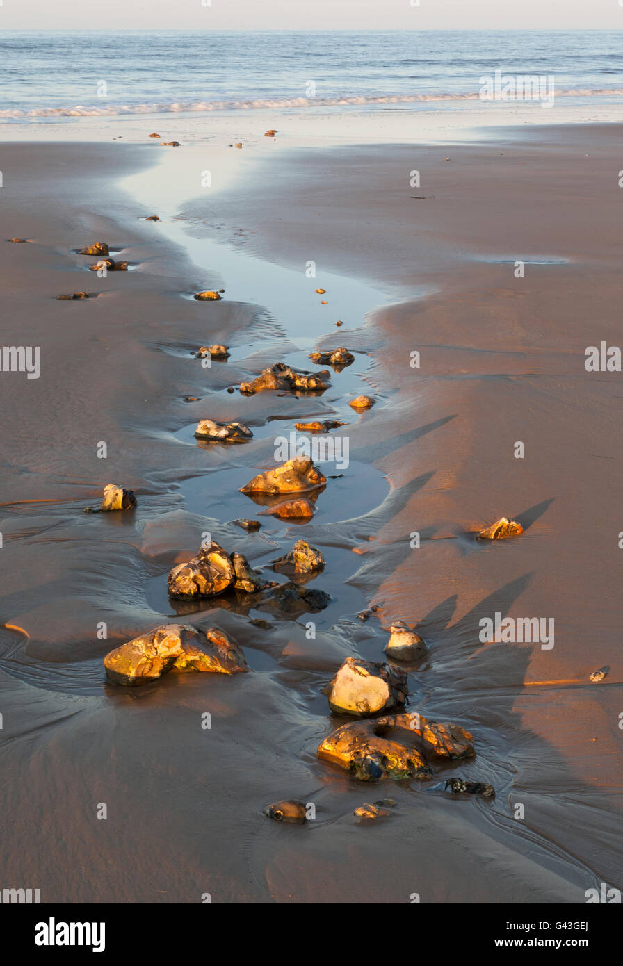 An inlet of water from the sea strewn with rocks on a sandy beach. UK Stock Photo