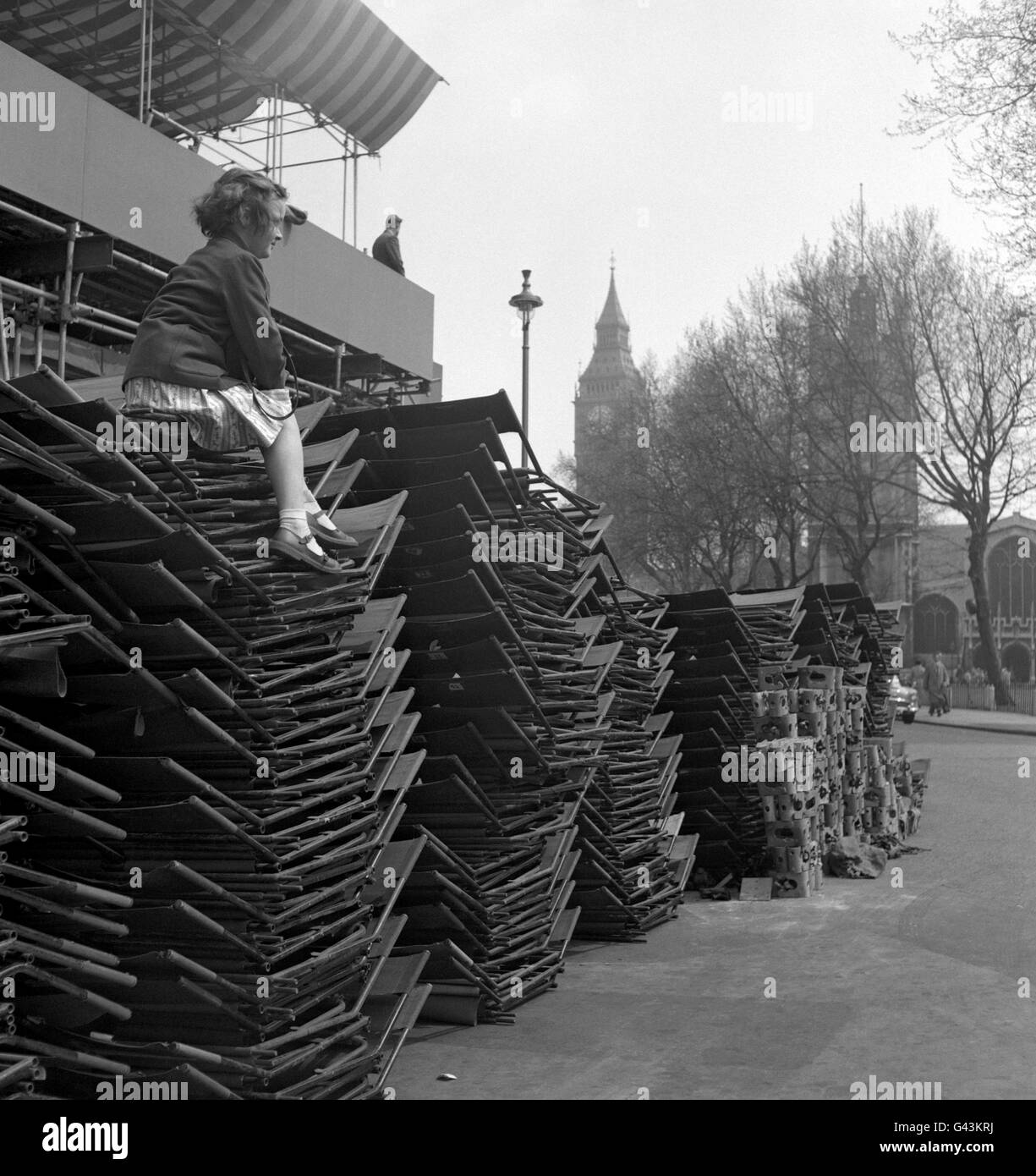 Nine-year-old Susan Lewey, of New Malden, sits on top of stacked chairs outside Westminster Abbey, London. As the wedding of Princess Margaret and Antony Armstrong-Jones draws nearer, decorations are going up along the Processional Route. Stock Photo