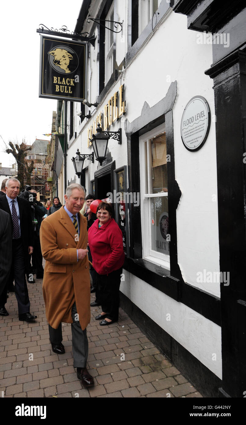 Prince Charles walks past the Black Bull pub in Cockermouth with a plaque on the right showing the flood levels reached in 2009. Stock Photo
