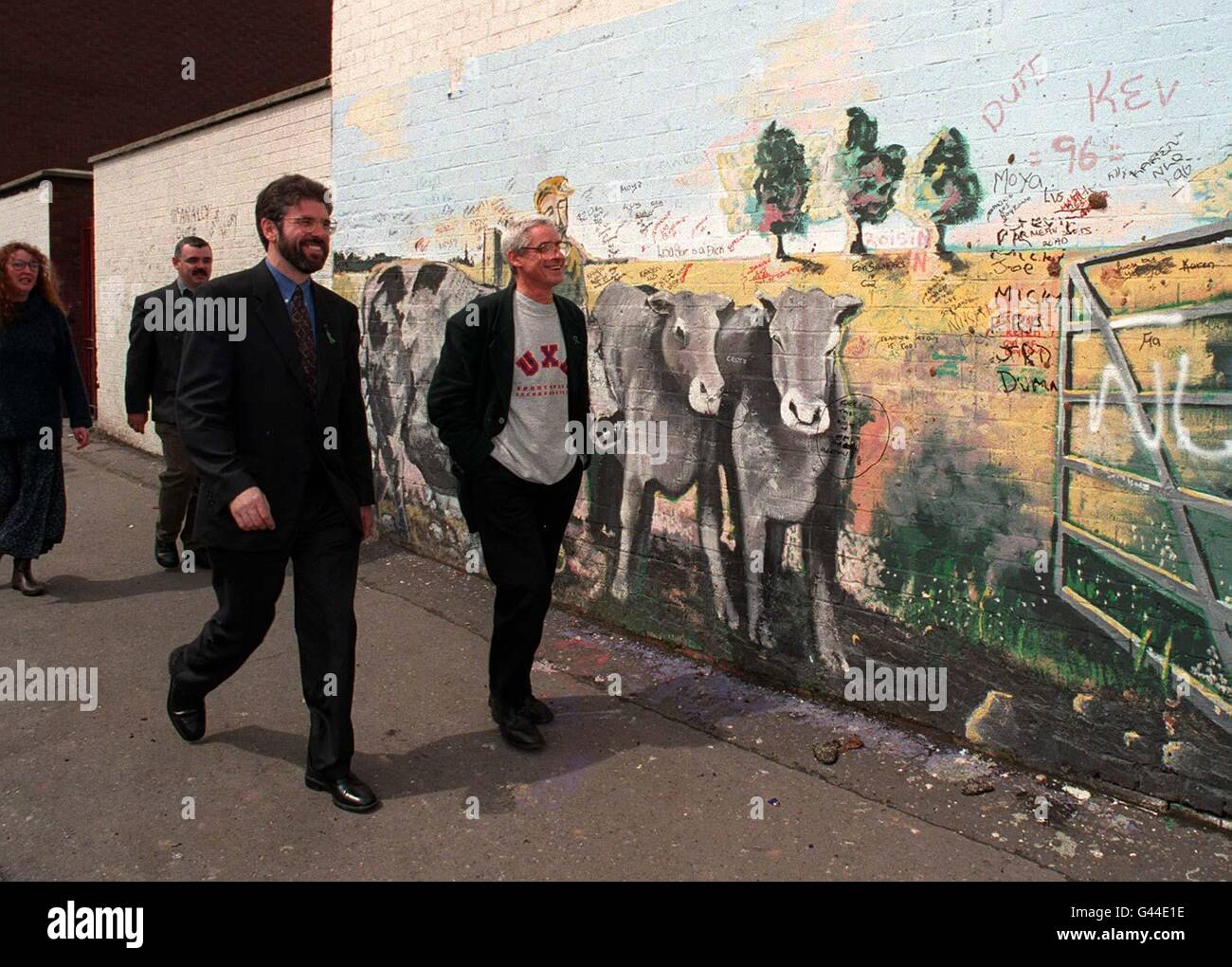 Troublesome picture for the British Government with Sinn Fein President Gerry Adams (left foreground) in the forefront of the Irish stalemate walking past a mural of cattle in North Belfast. Stock Photo