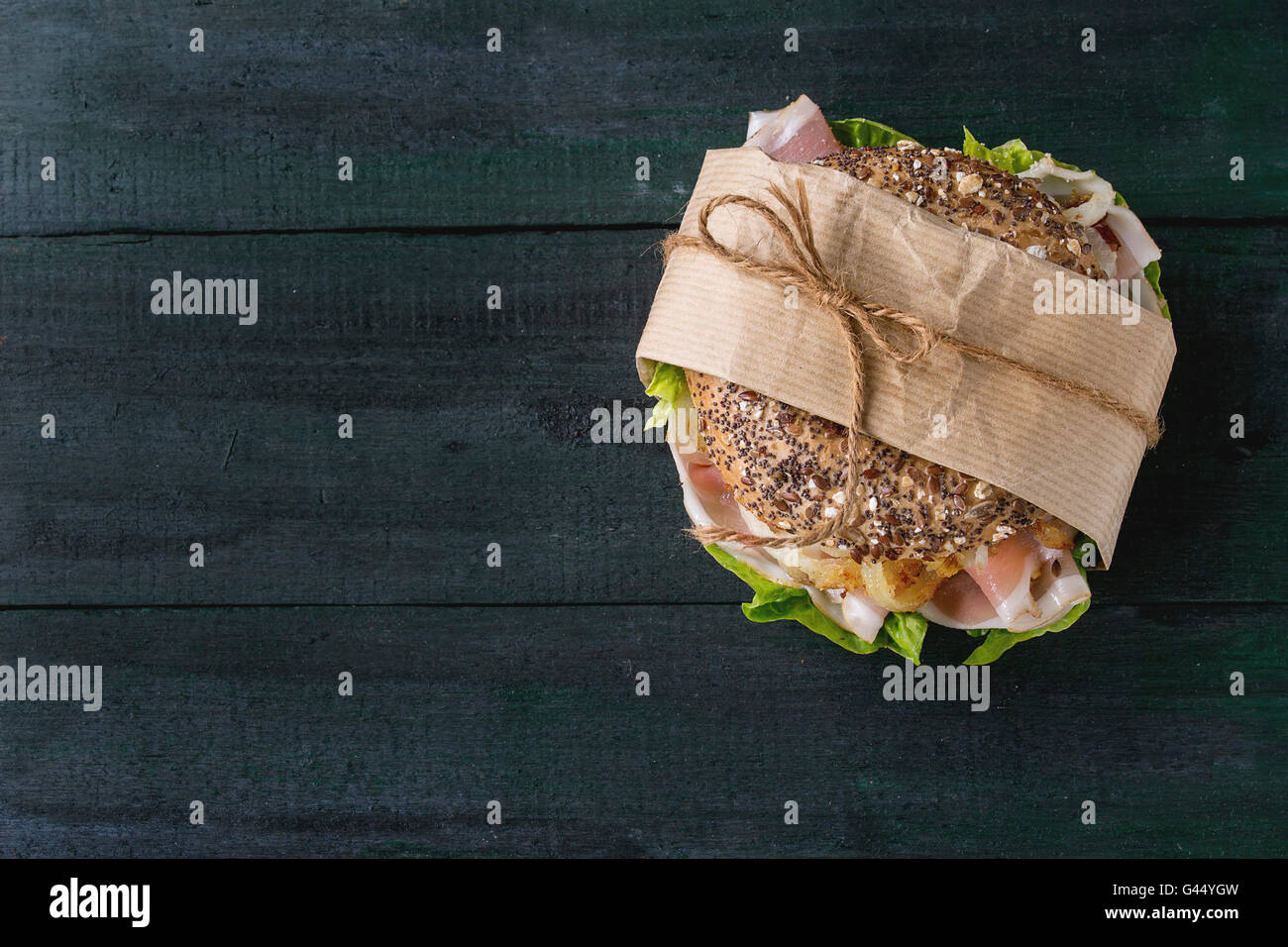 Papered Whole Grain bagel with fried onion, green salad and prosciutto ham over dark wooden textured background. Top view Stock Photo