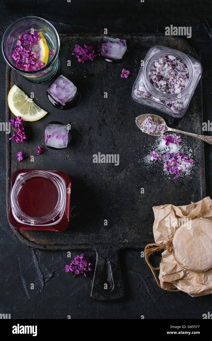 Lilac products collection. Glass jar of lilac flowers in sugar,glass of lilac water with lemon, ice cubes with flowers and jar o Stock Photo