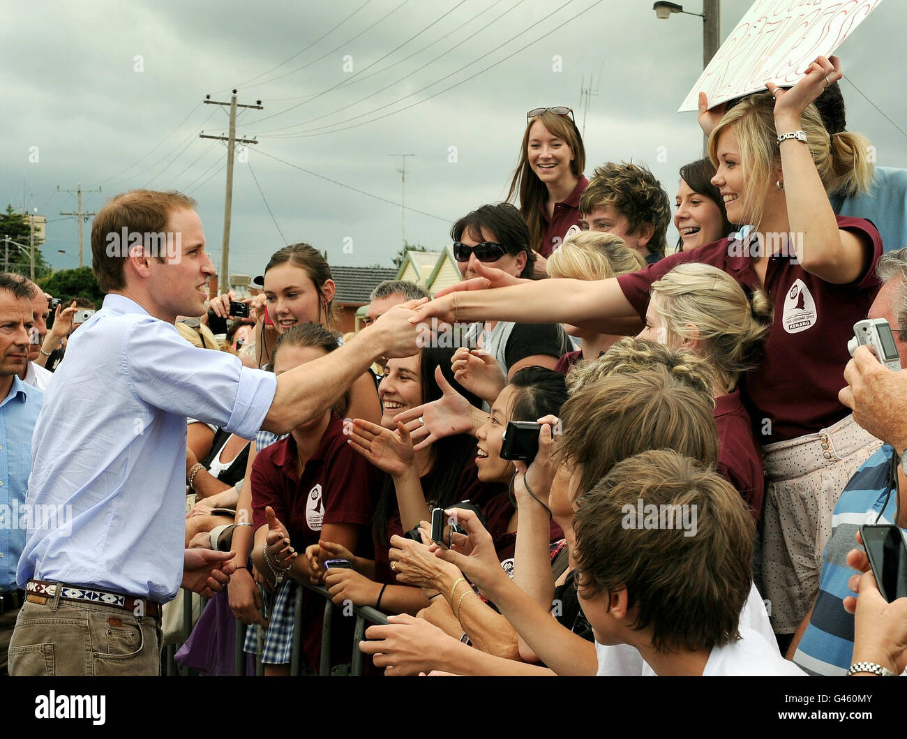 Tiana O'Brien shakes hands with Prince William whilst holding a sign reading: 'I'll be your princess' only to be told by him 'Sorry, you're too late' during a walkabout in Kerang southern Australia, on the last day of his visit to New Zealand and Australia. Stock Photo