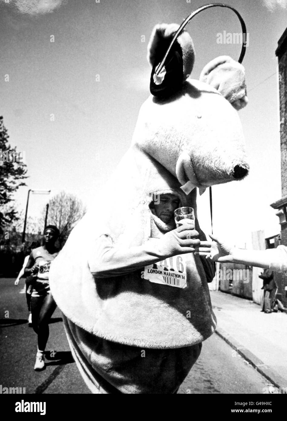A runner in costume drinking a pint of beer during the London Marathon Stock Photo