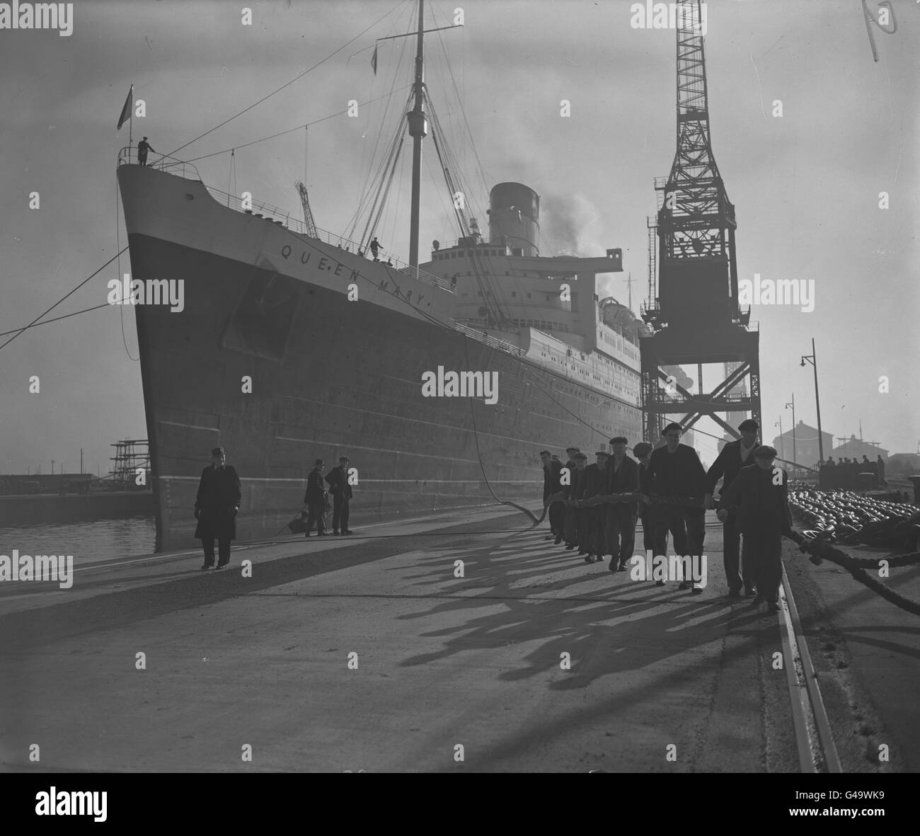 The 81,000 ton Cunard-White Star liner RMS Queen Mary moves in stately manner into the King George V dry dock in Southampton for her annual overhaul, aided by a long line of dockworkers on the rope. Stock Photo