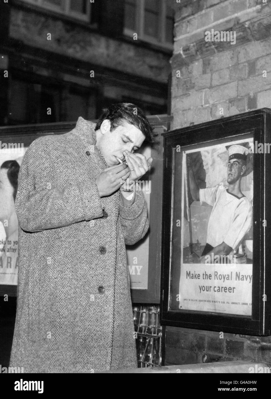 BESIDE A RECRUITING POSTER, ROCK'N'ROLL SINGER MARTY WILDE PAUSES TO LIGHT A CIGARETTE AS HE ARRIVES FOR HIS NATIONAL SERVICE MEDICAL EXAMINATION AT LEE ROAD, SOUTH LONDON TODAY. Stock Photo