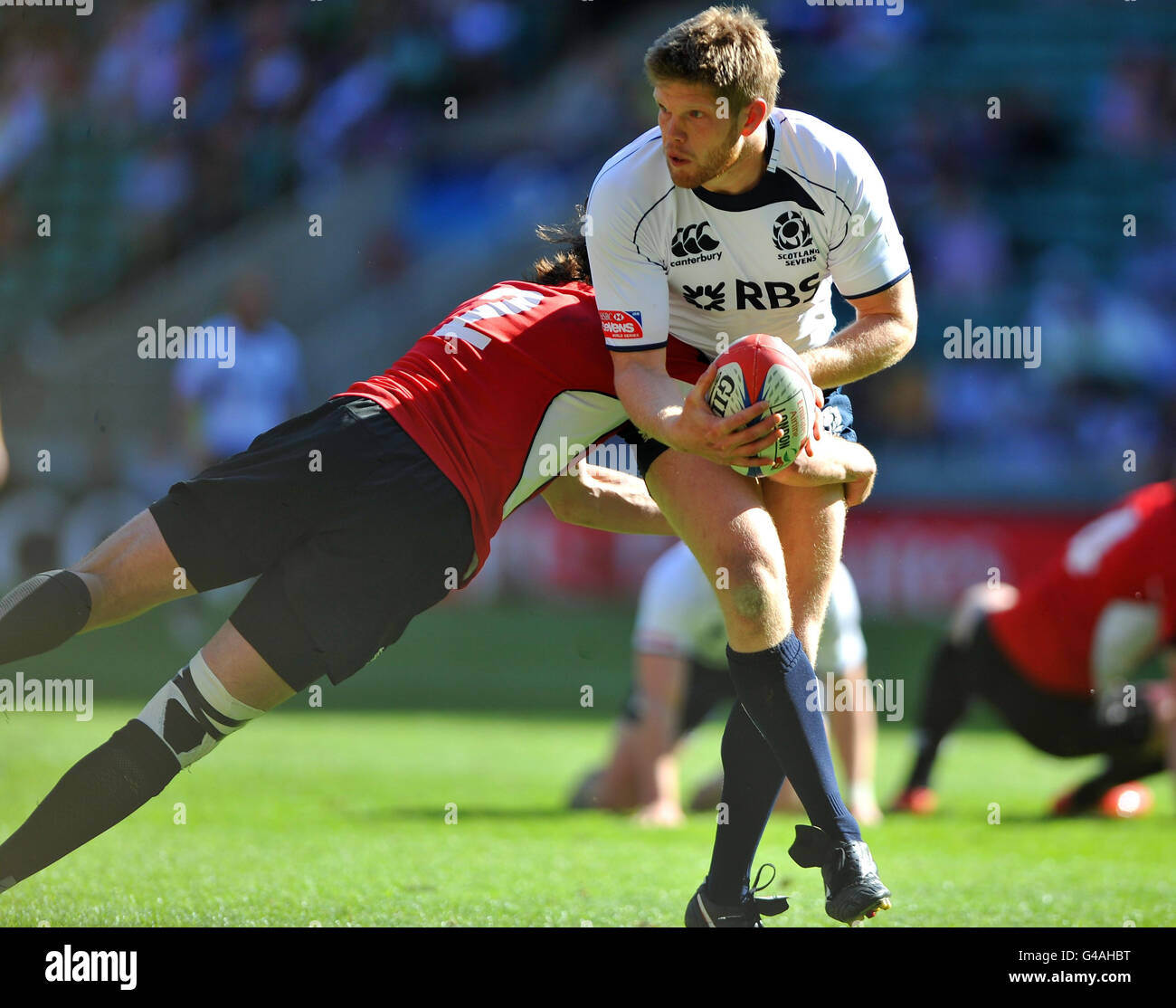 Scotland's Scott Newlands (right) is tackled by Canada's Thyssen de Goede during the match 17 of the IRB Emirates Airline London Sevens at Twickenham Stadium, London. Stock Photo
