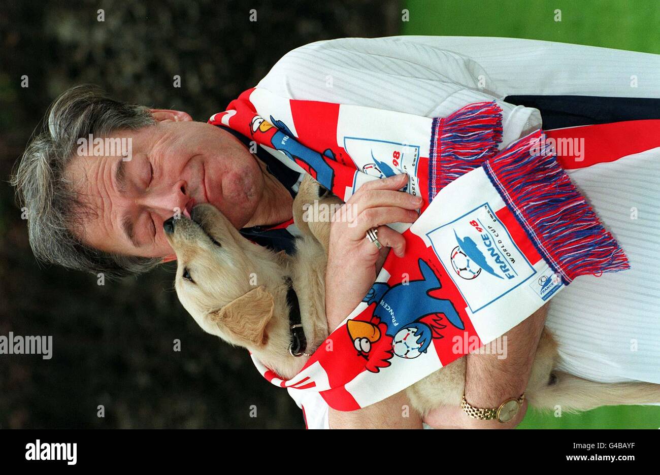 Sports Minister Tony Banks is licked by 7-month-old Golden Retriever, Rye, as he kicked off the world's largest auction of signed football shirts to raise money for training guide dogs for the blind, in London today (Weds). Mr Banks, pictured wearing an England shirt and scarf, launched the Put Your Shirt On a Dog Campaign, which is expected to raise at least 50,000 for The Guide Dogs for the Blind Association. See PA Story CHARITY Blind. Photo by Fiona Hanson. Stock Photo