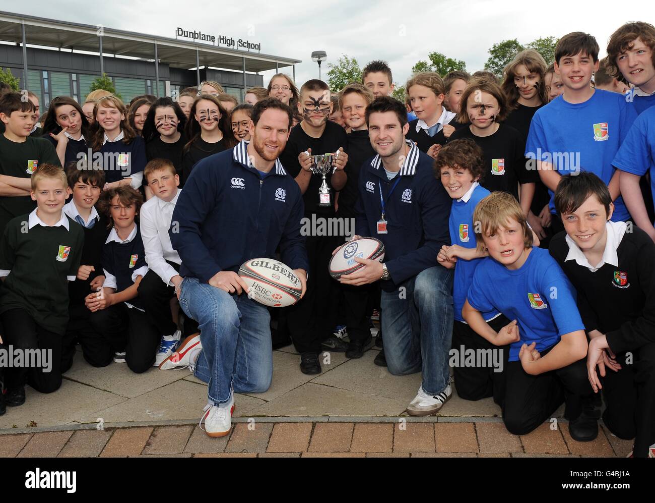 Dunblane High School held their own Rugby World Cup this week with teams representing the 7 nations as Scotland stars Johnny Beattie and Graeme Morrison (left) went along to present the trophy to winning team captain Jim Brownlee (centre) representing New Zealand, team pictured with all the kids taking part, during the World Cup photocall at Dunblane High School, Dunblane. Stock Photo