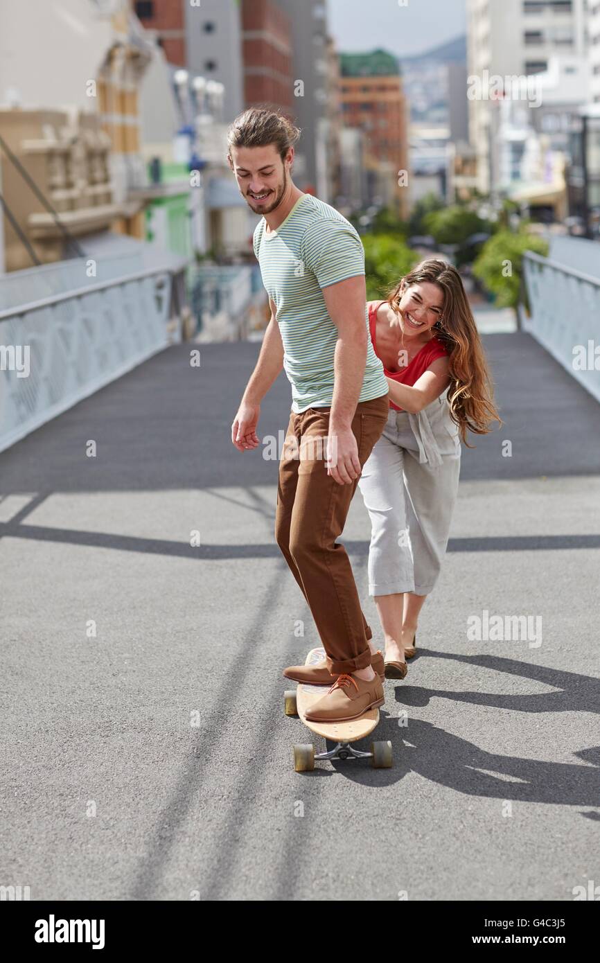 MODEL RELEASED. Young man skateboarding with woman pushing. Stock Photo