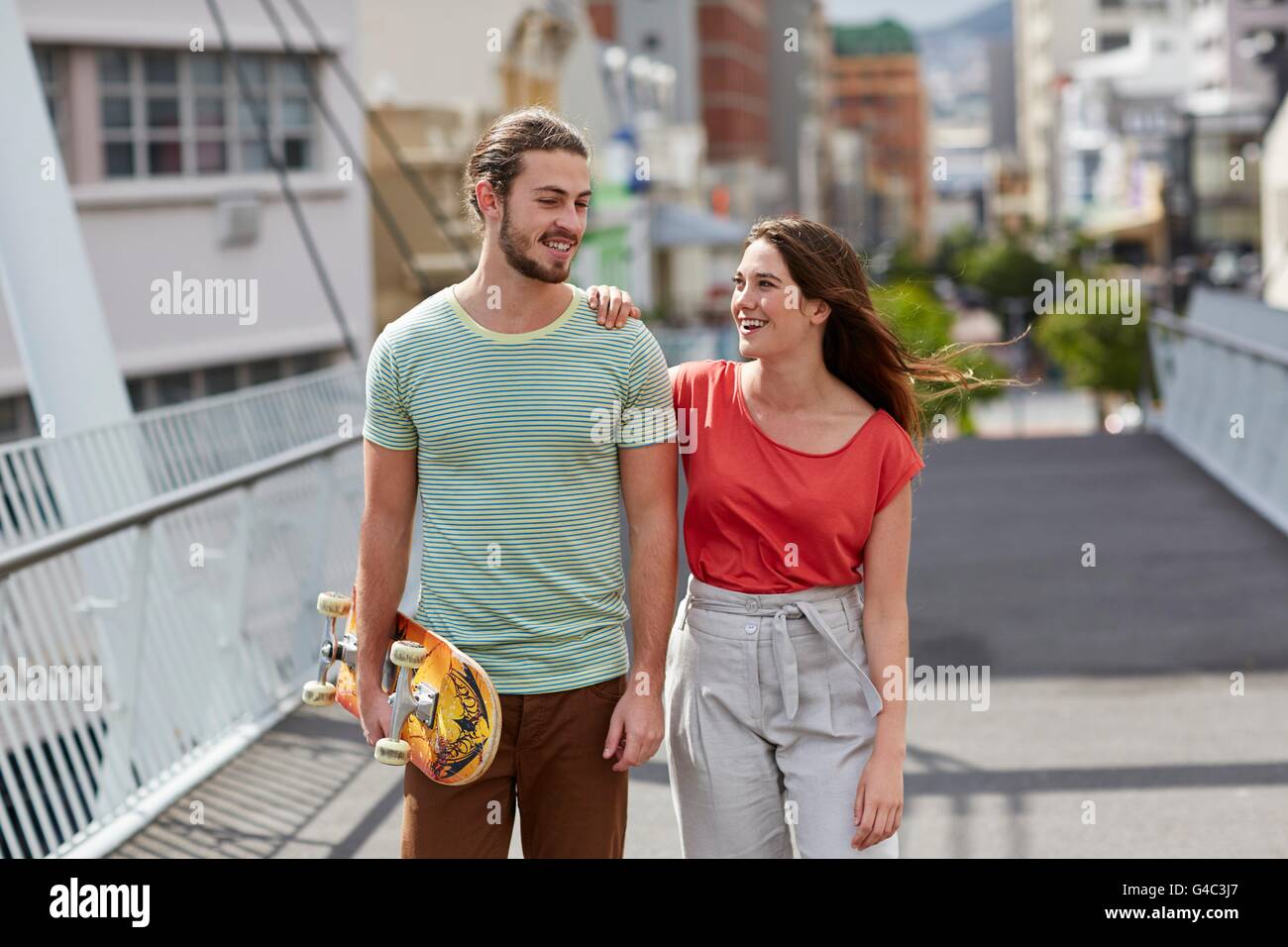 MODEL RELEASED. Young couple walking, man carrying skateboard. Stock Photo