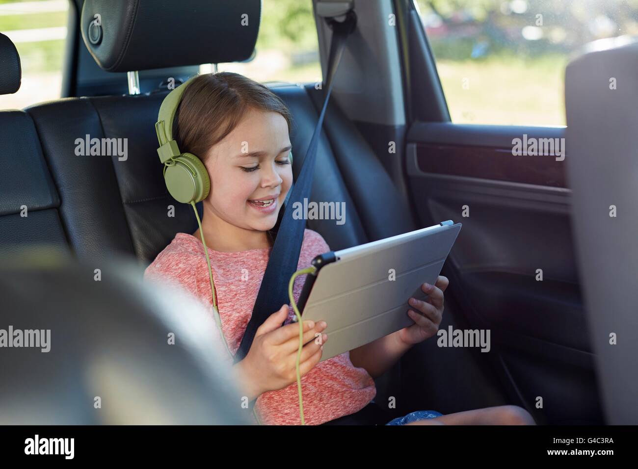 MODEL RELEASED. Girl in the back seat of the car wearing headphones, watching a movie. Stock Photo