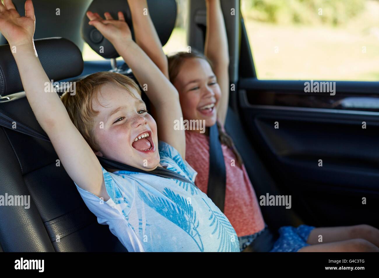MODEL RELEASED. Brother and sister in the back seat of the car with arms raised. Stock Photo