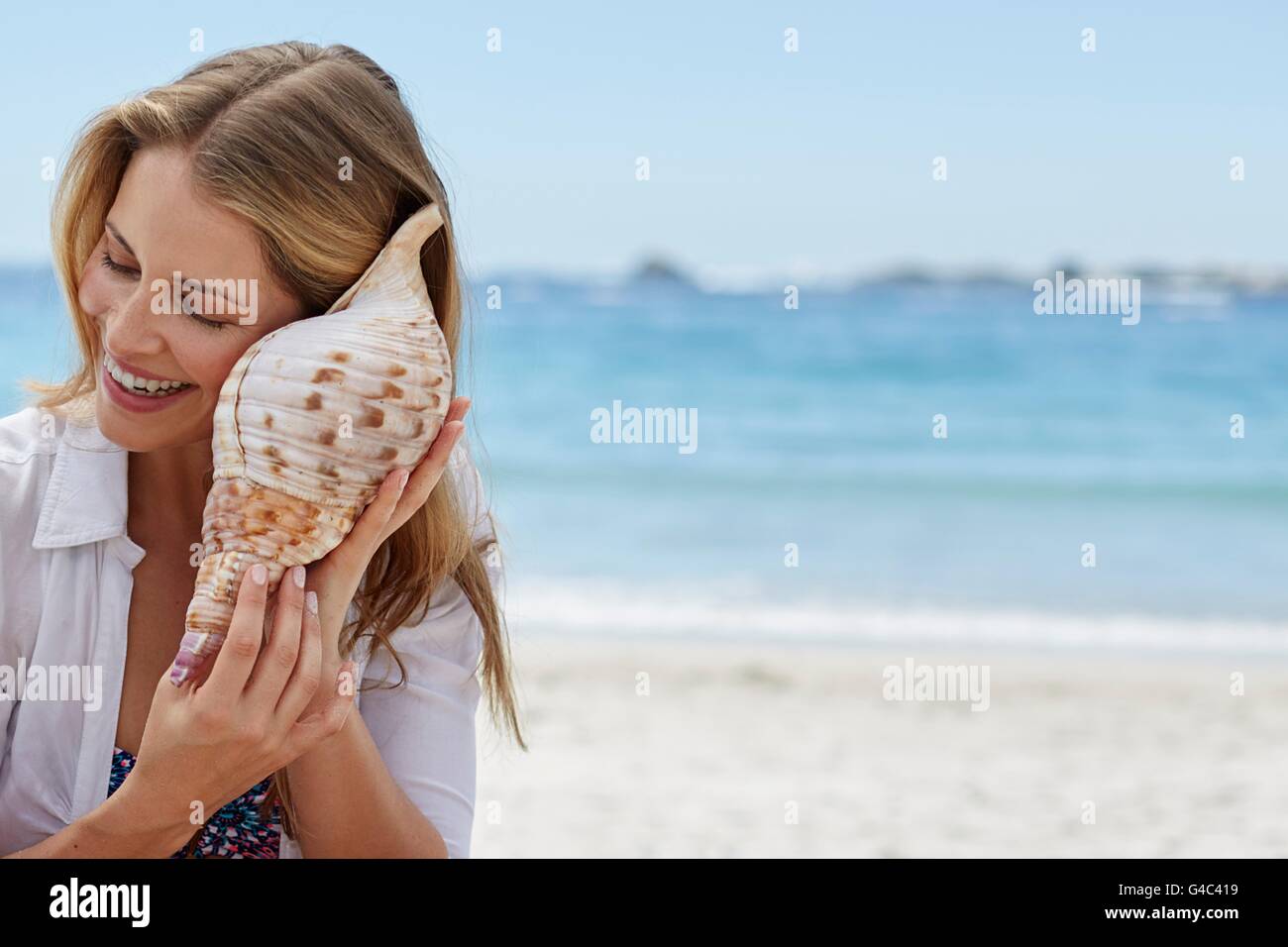 MODEL RELEASED. Young woman listening to a seashell. Stock Photo