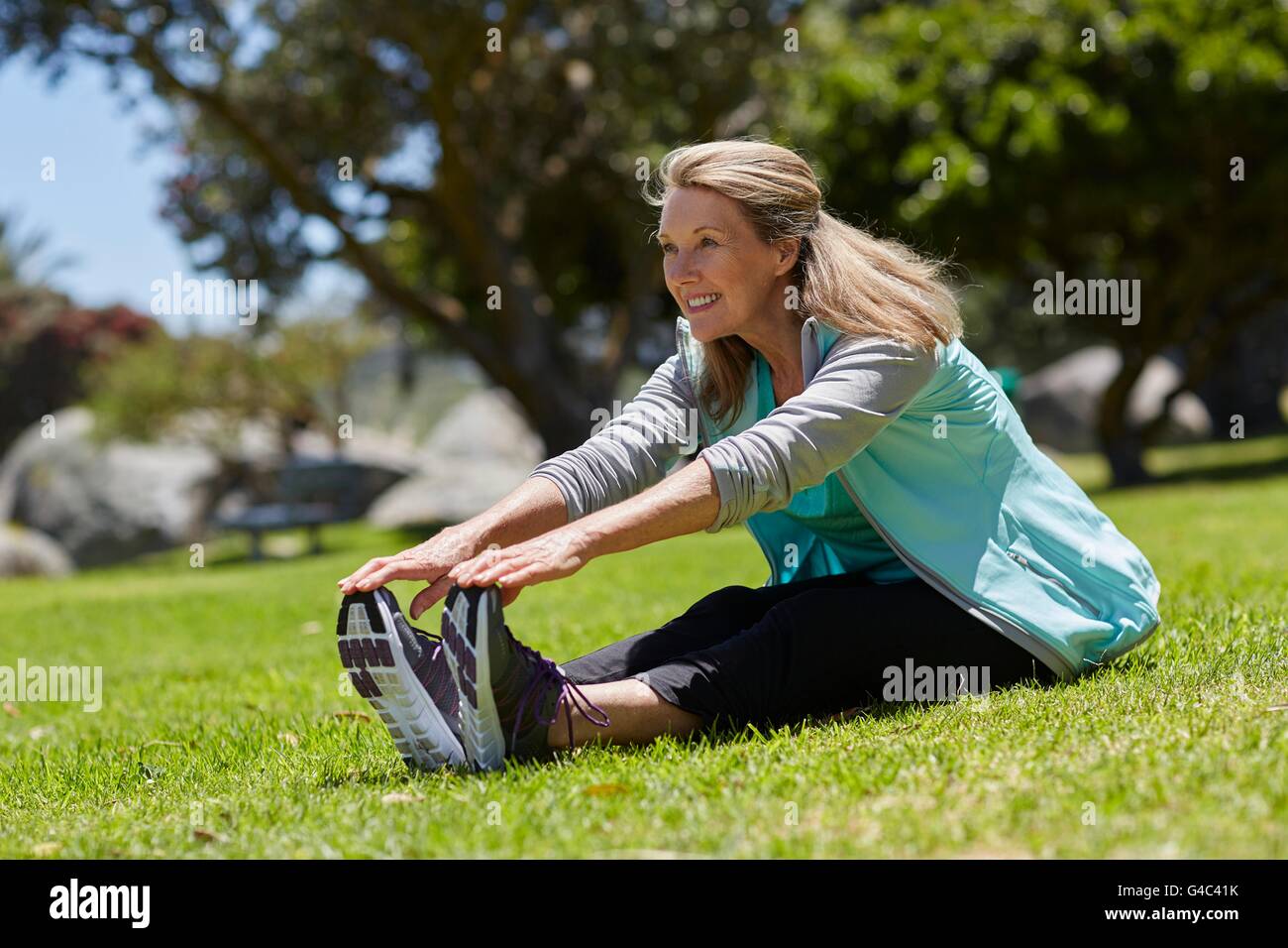 MODEL RELEASED. Senior woman stretching on grass. Stock Photo