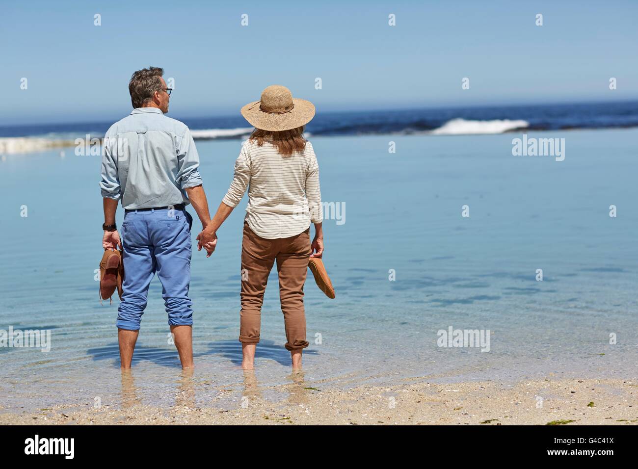 MODEL RELEASED. Senior couple holding hands, paddling in the sea. Stock Photo