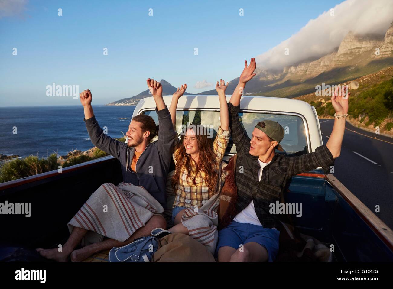 MODEL RELEASED. Young friends in pick up truck with arms raised, Stock Photo