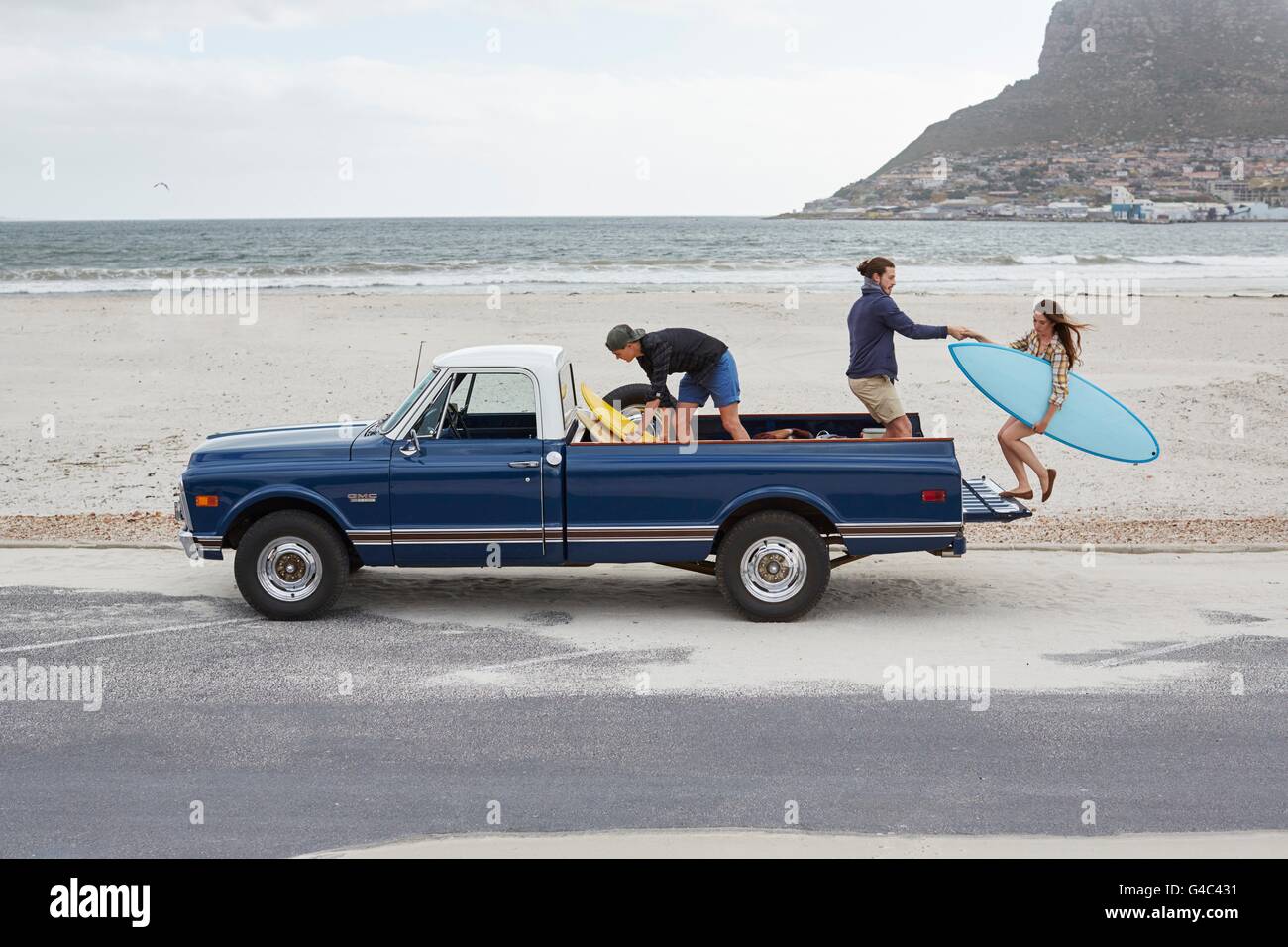 MODEL RELEASED. Young woman with surfboard being helped up into pick up