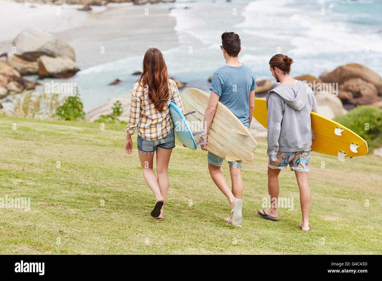 MODEL RELEASED. Three young adults walking towards beach with surfboards. Stock Photo