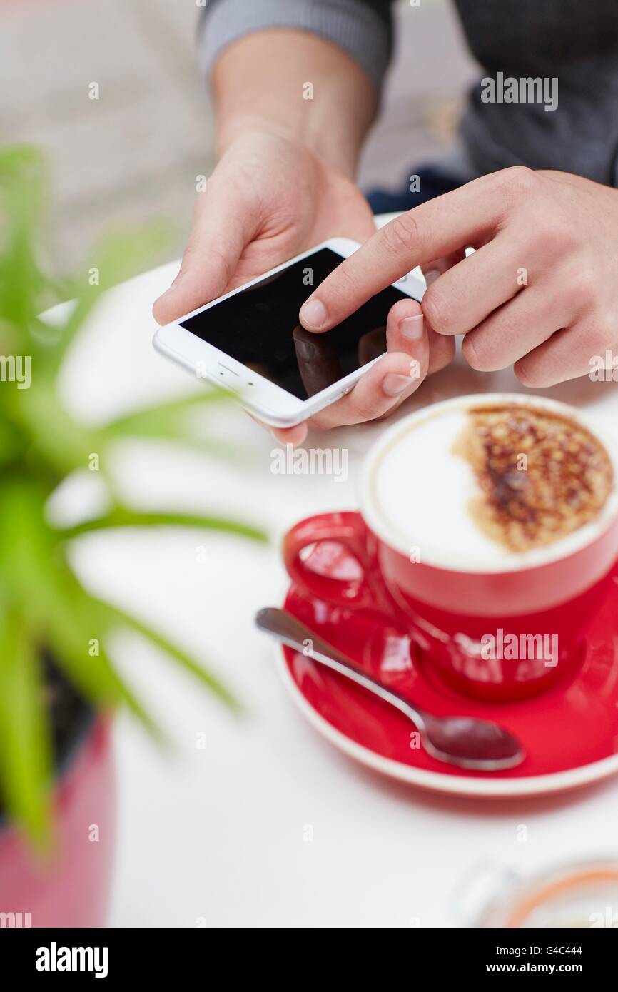 MODEL RELEASED. Person using smartphone with coffee, close up. Stock Photo