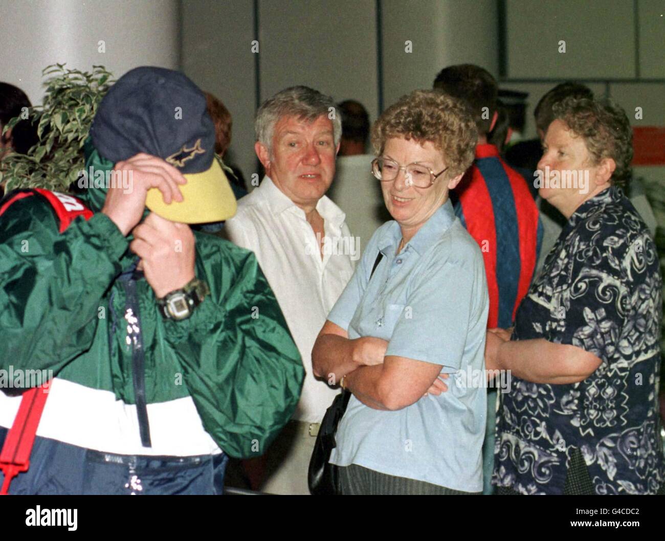 Tourists throw a disdainful look at a soccer fan as he hides his face from the cameras on his arrival back at Glasgow Airport from Salou in eastern Spain today (Saturday) where trouble broke out amongst fans after they were refused entry to France. French police acting on a 'tip-off' stopped a coach-load of fans heading for Bordeaux where Scotland played Norway earlier this week as it tried to cross into France at the Spanish border. See PA story SPORT Cup Scots. Photo by David Cheskin/PA Stock Photo