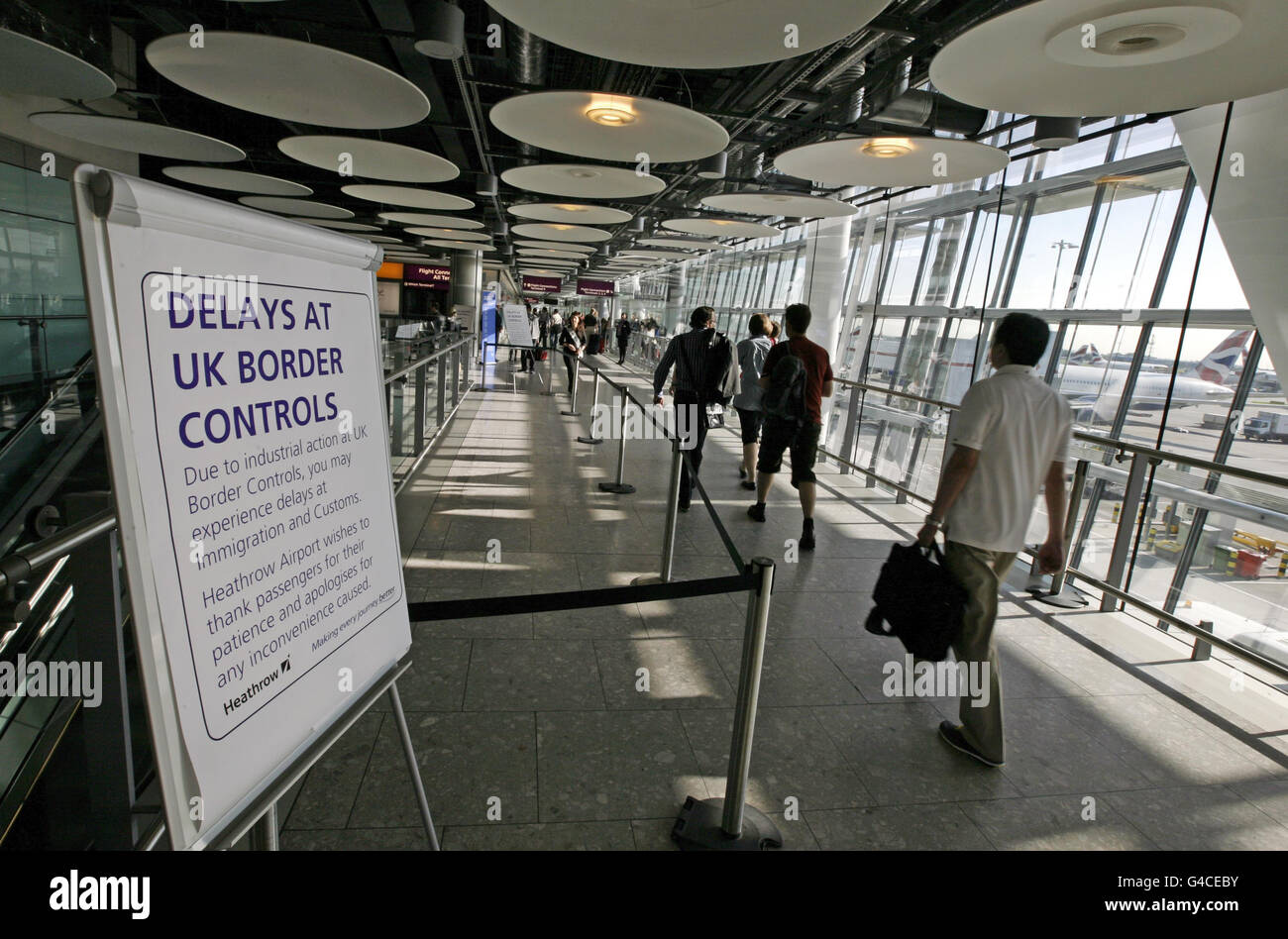 Passengers walk past an information sign in arrivals at Border Control in Terminal Five of London's Heathrow Airport where some immigration and customs staff have joined a day of strikes by teachers, civil servants and other workers over Government plans to change their pensions, cut jobs and freeze pay. Stock Photo