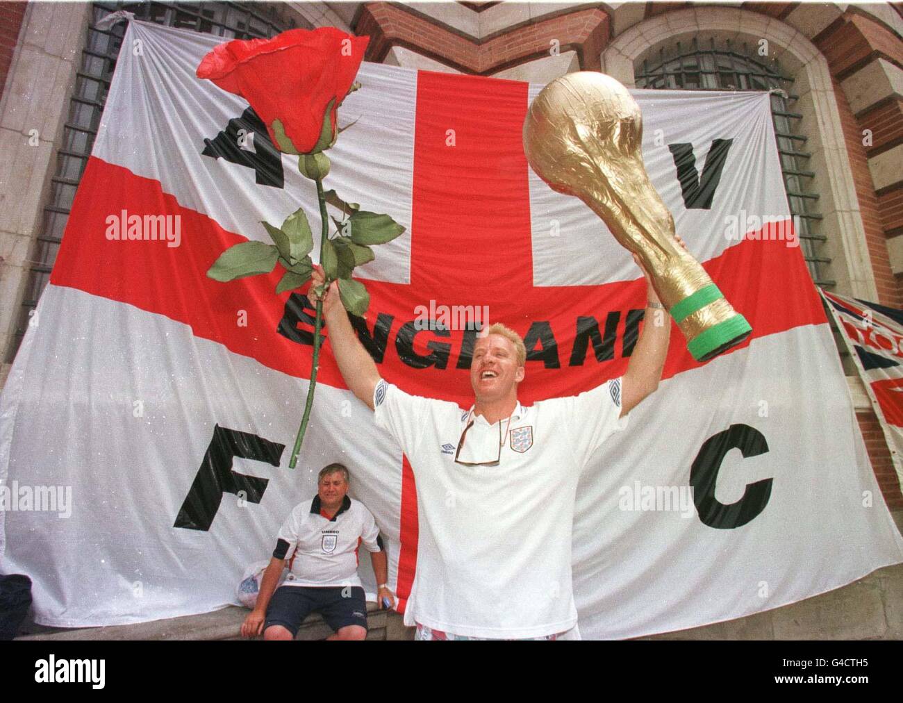 Patriotic English Soccer fan, Ashley White, stands in front of a huge flag of St George hoisted onto the wall of the Town Hall in Toulouse today (Monday) as he holds aloft a giant English rose and a model of the World Cup Trophy. Thousands of fans were gathering in the centre of the French city where England face their second clash of tournament against Romania later this evening. Photo by Peter Jordan/PA Stock Photo