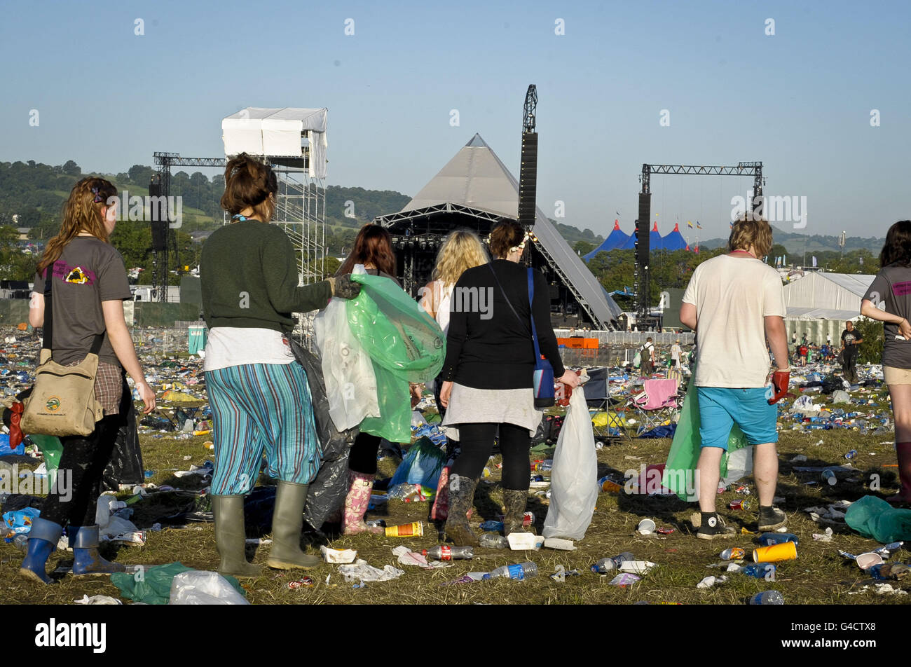 Litter pickers walks past the area in front of the Pyramid stage as it is littered with rubbish and waste as Glastonbury festival at Worthy Farm, Pilton draws to a close. Stock Photo