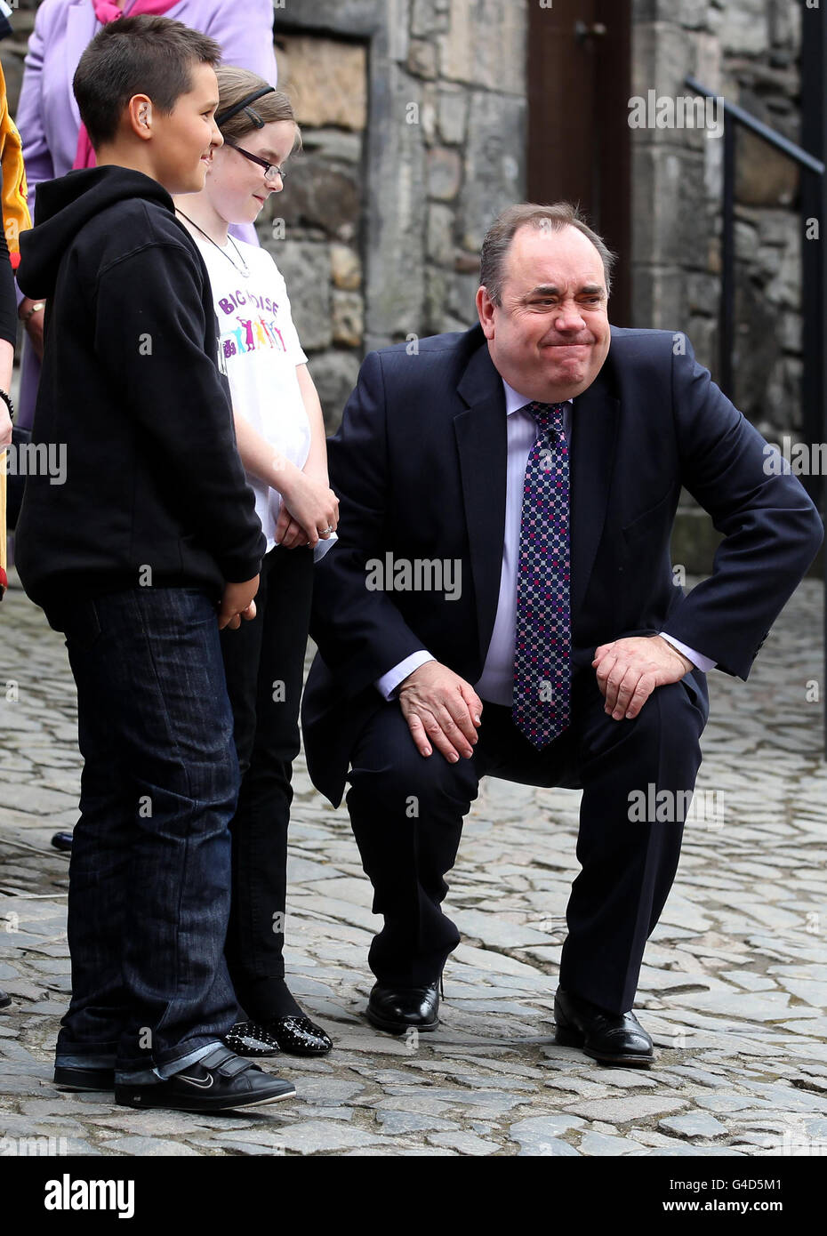 Scotland's First Minister Alex Salmond, reacts as he gets back to his feet after crouching down to talk with children from the Big Noise group who performed for Queen Elizabeth II, during a visit to Stirling Castle where the Queen re-opened the James V Palace at the castle, following a 12 million project which has returned the six apartments in the castle's Renaissance palace to how they may have looked in the mid-16th century. Stock Photo